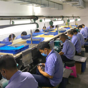 Workers inspecting parts in electronics manufacturing line.