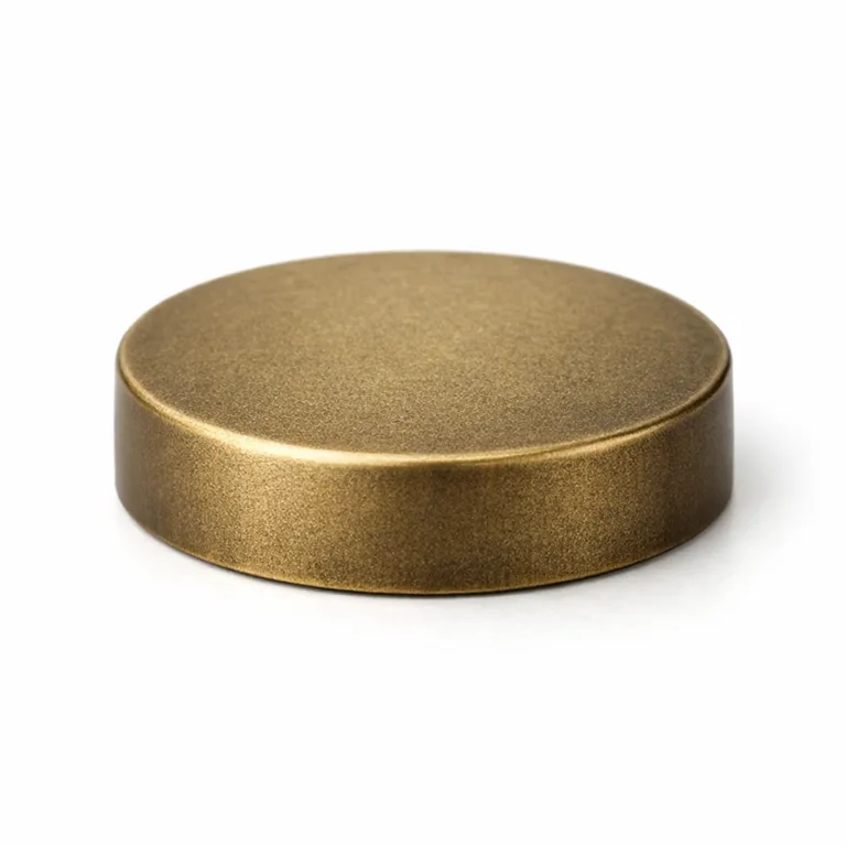A sandblasted matte finish antique brass bottle cap with a flat edge, imaged with clear, commercial lighting for maximum detail. The subdued metallic look offers a modern, sophisticated bottle accessory.