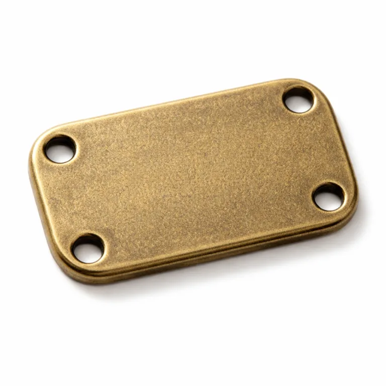 Close-up studio image of an antique brass finish sew-on brand tag with a sandblasted matte texture, softly rounded rectangular edges, and four sewing holes, designed for secure sewing onto products.