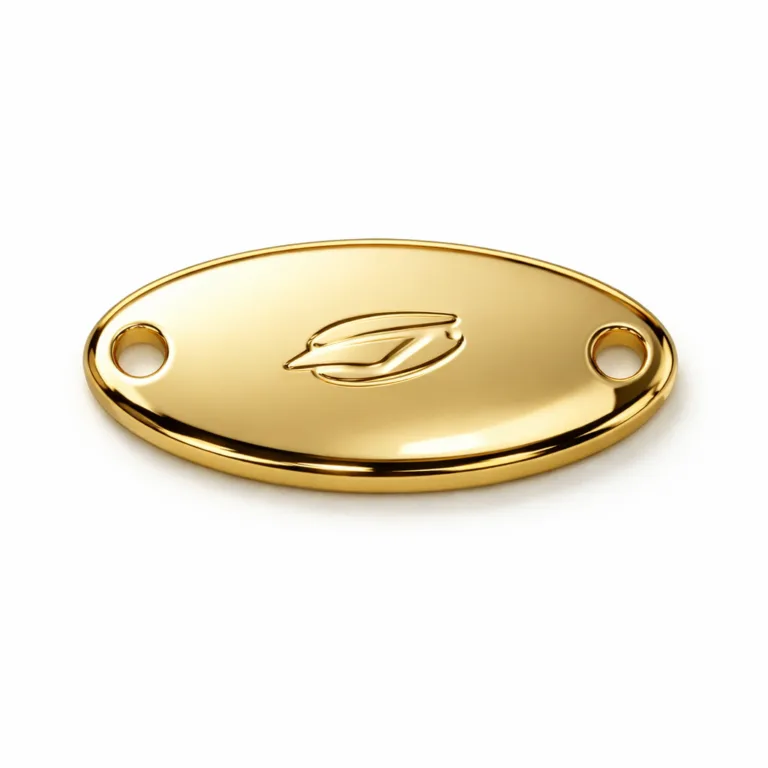 High realism studio product photo of a gold-plated, oval-shaped sew-on metal brand tag, mirror polished finish, with two sewing holes at the ends and a subtle unbranded 2D relief emblem feature.