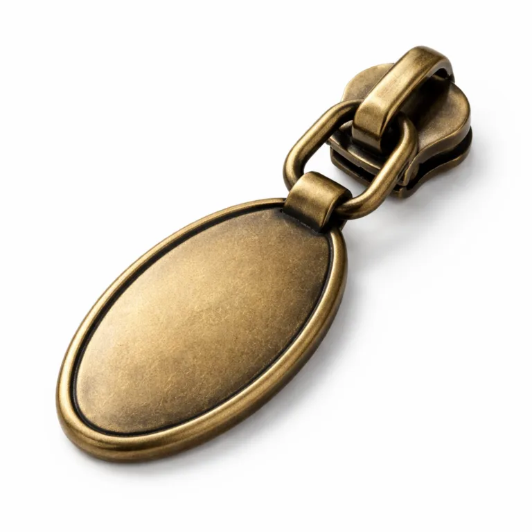 Studio product image featuring an oval stamped zipper pull plate in brass with an antique brass finish and soft, rounded edges, emphasizing a vintage and classic style suitable for retro fashion.