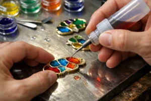 A skilled craftsman fills a metal pin mold with vibrant translucent enamel, capturing the glowing stained glass effect under professional lighting, highlighting quality and color clarity.