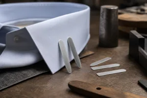 A close-up manufacturing scene showing premium metal collar stays and shirt collar fit context.